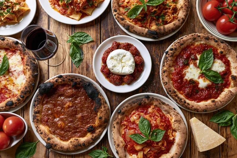 Overhead view of an italian restaurant table spread with pizzas, pasta, wine, and fresh ingredients