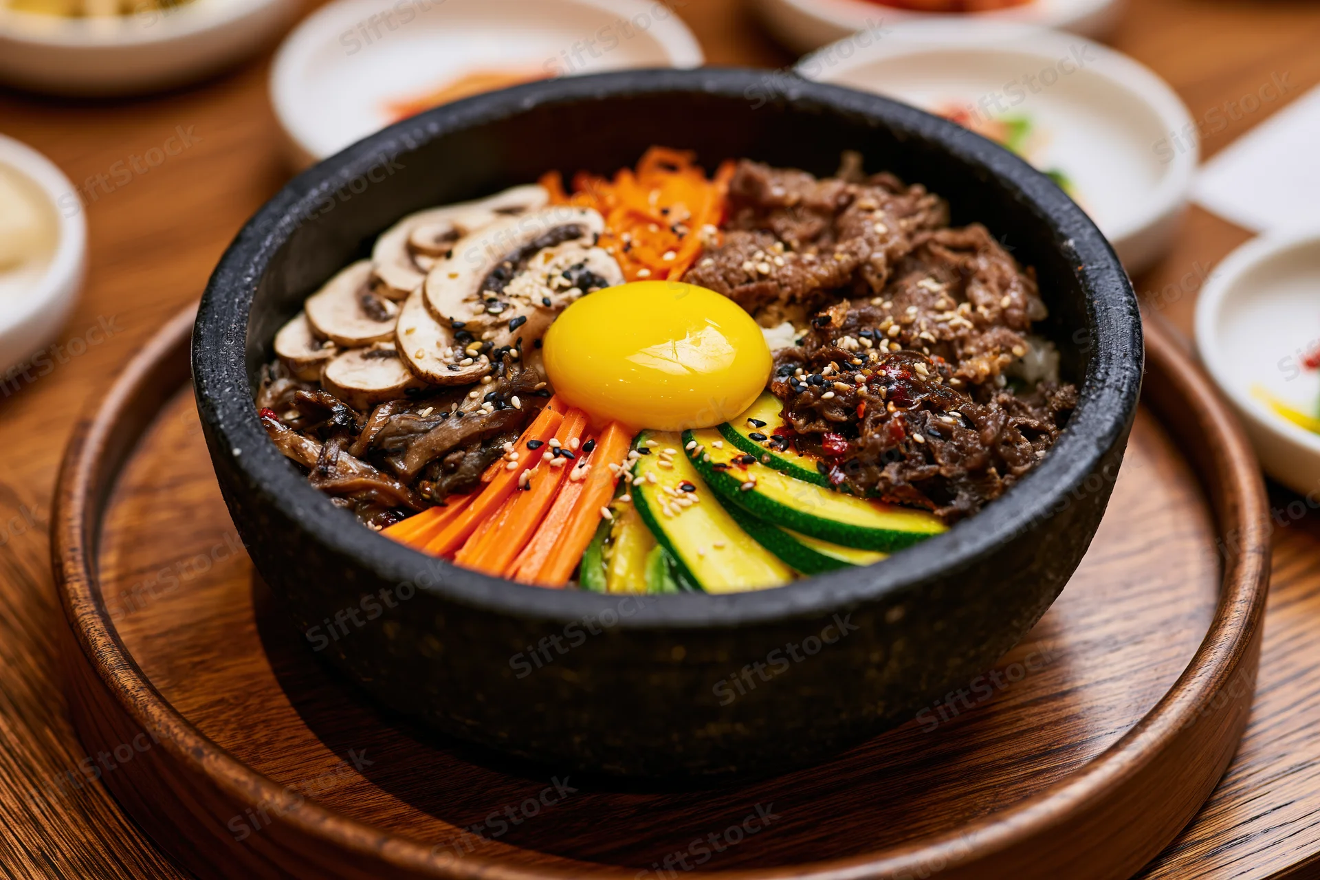 Korean bibimbap in a black stone bowl with beef, vegetables and egg on a wooden tray