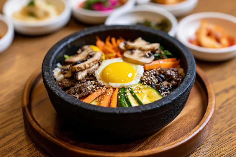 Korean bibimbap in a black stone bowl with beef, egg, vegetables and side dishes on a wooden table