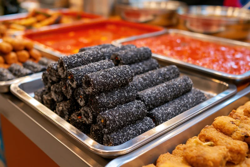 Black sesame rolls stacked on metal tray at korean street food stall counter