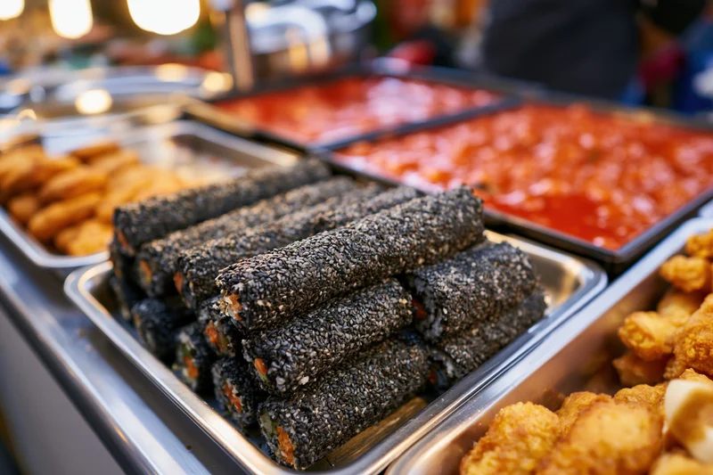 Black sesame-covered kimbap rolls arranged on metal trays at a korean street food stall counter