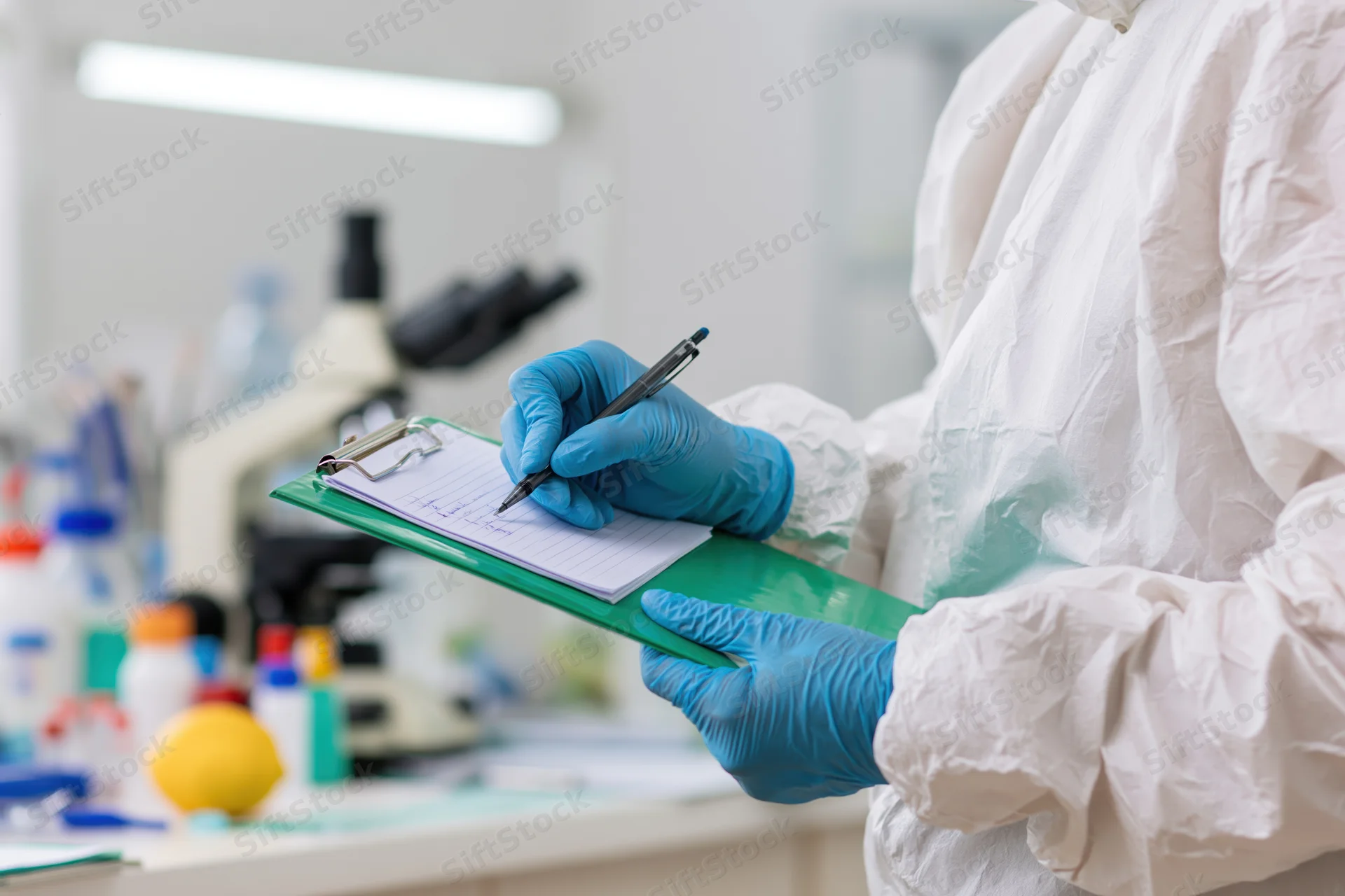 Scientist in white hazmat suit writing notes on clipboard in laboratory