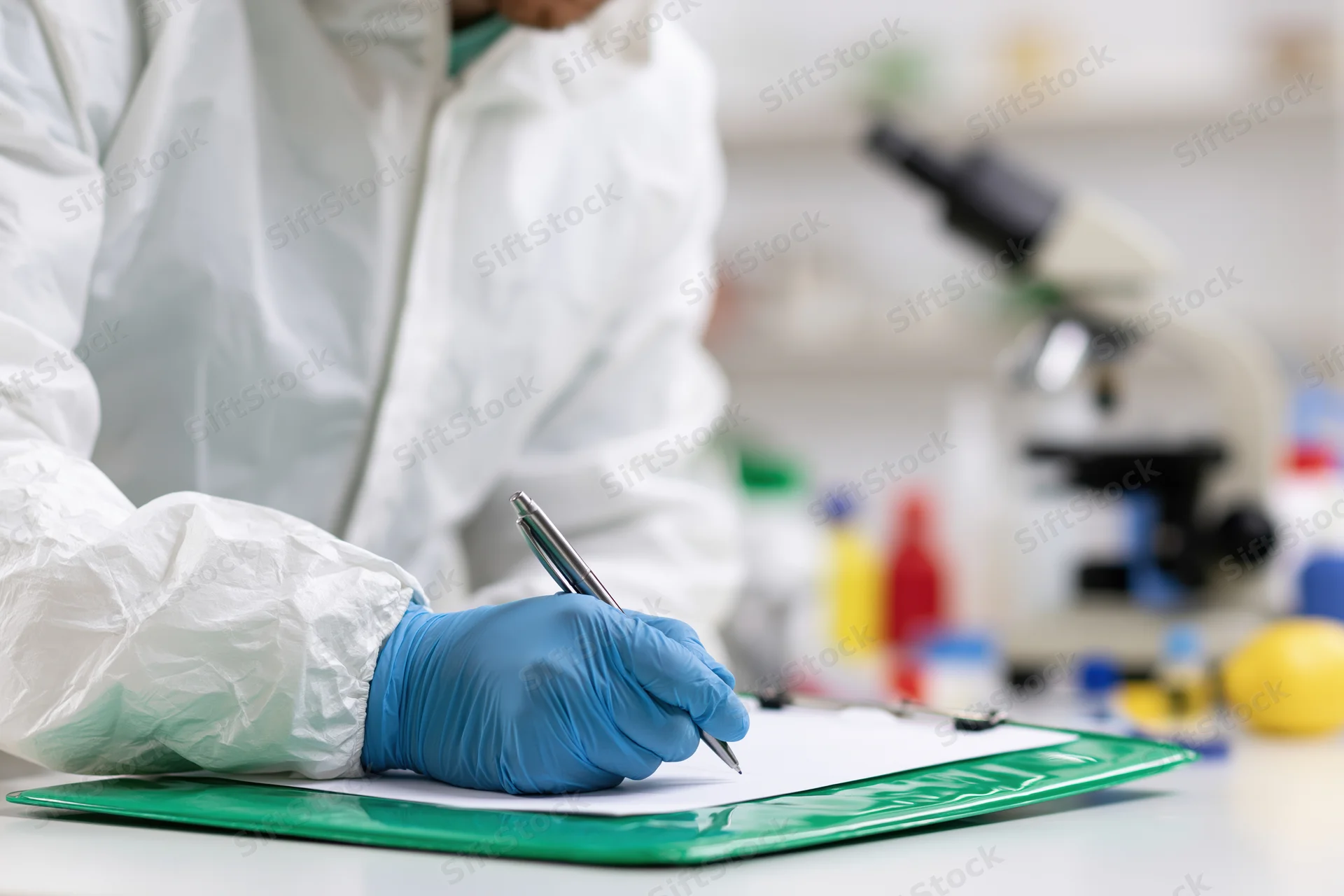 Lab technician in white hazmat suit writing on clipboard in laboratory