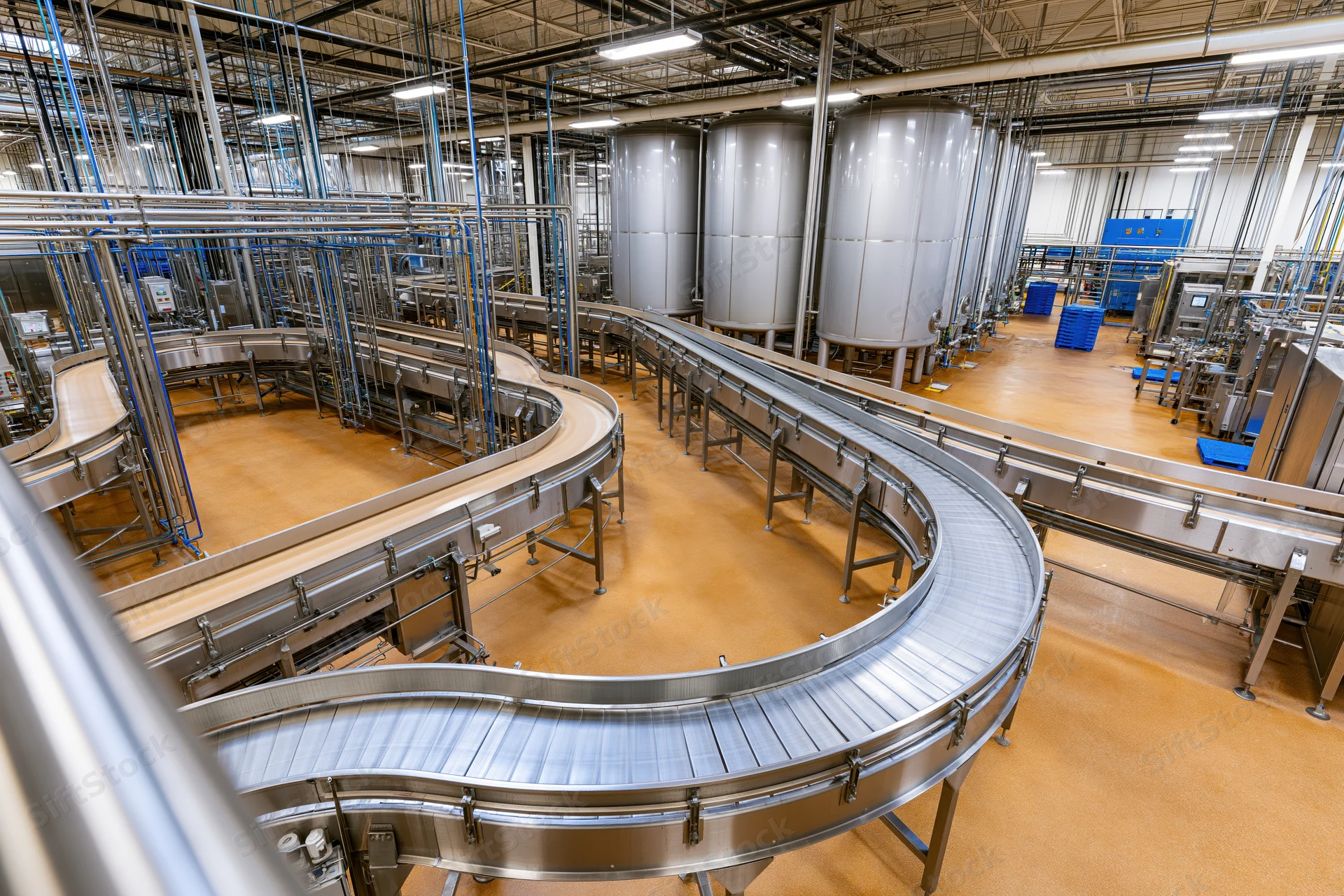 Curved stainless steel conveyor belts in a large food and beverage processing plant interior