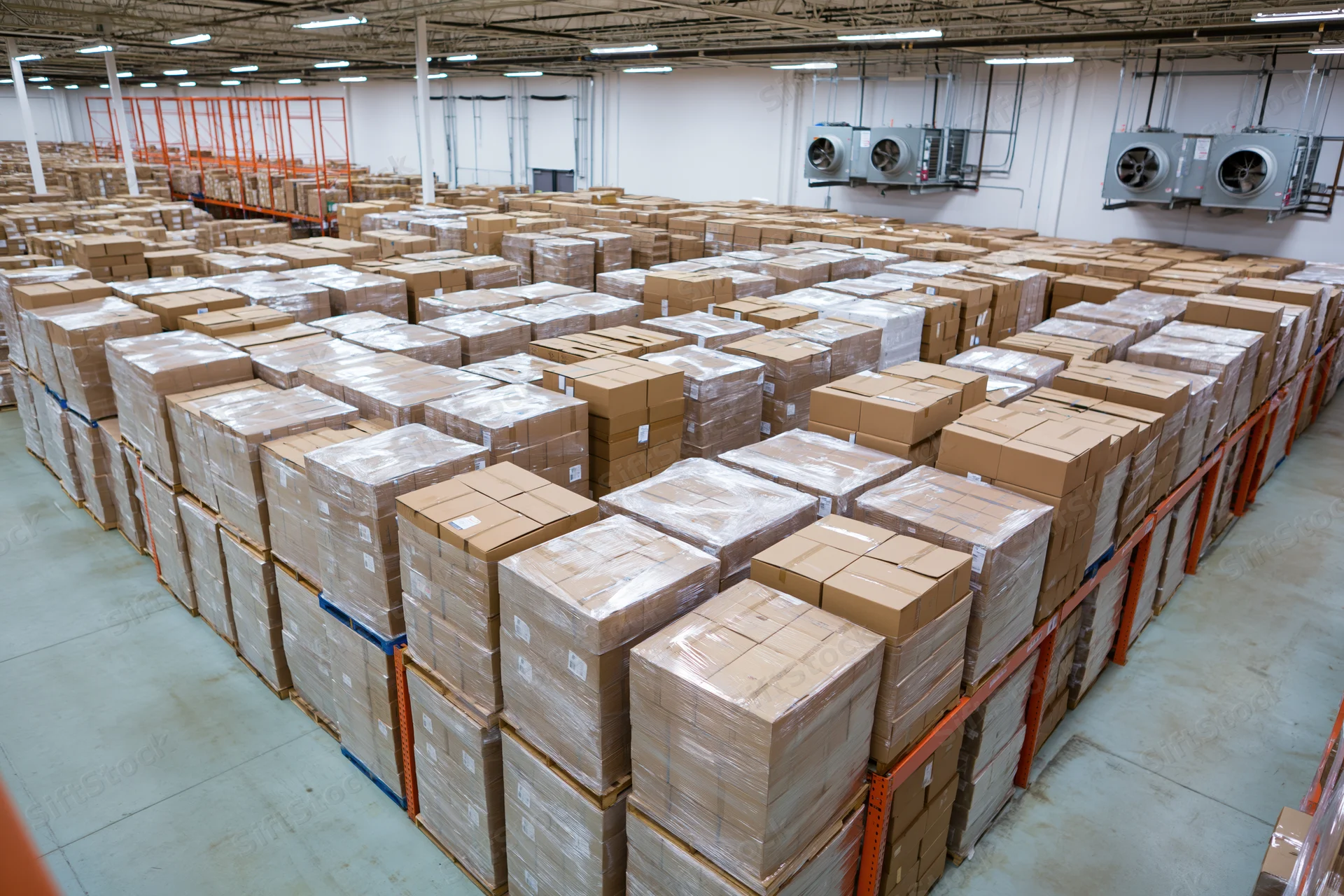 Rows of stacked cardboard boxes on pallets in a large commercial warehouse interior