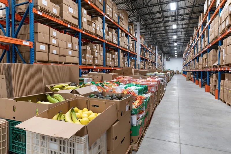Rows of stacked pallets with boxes of produce in a large warehouse aisle