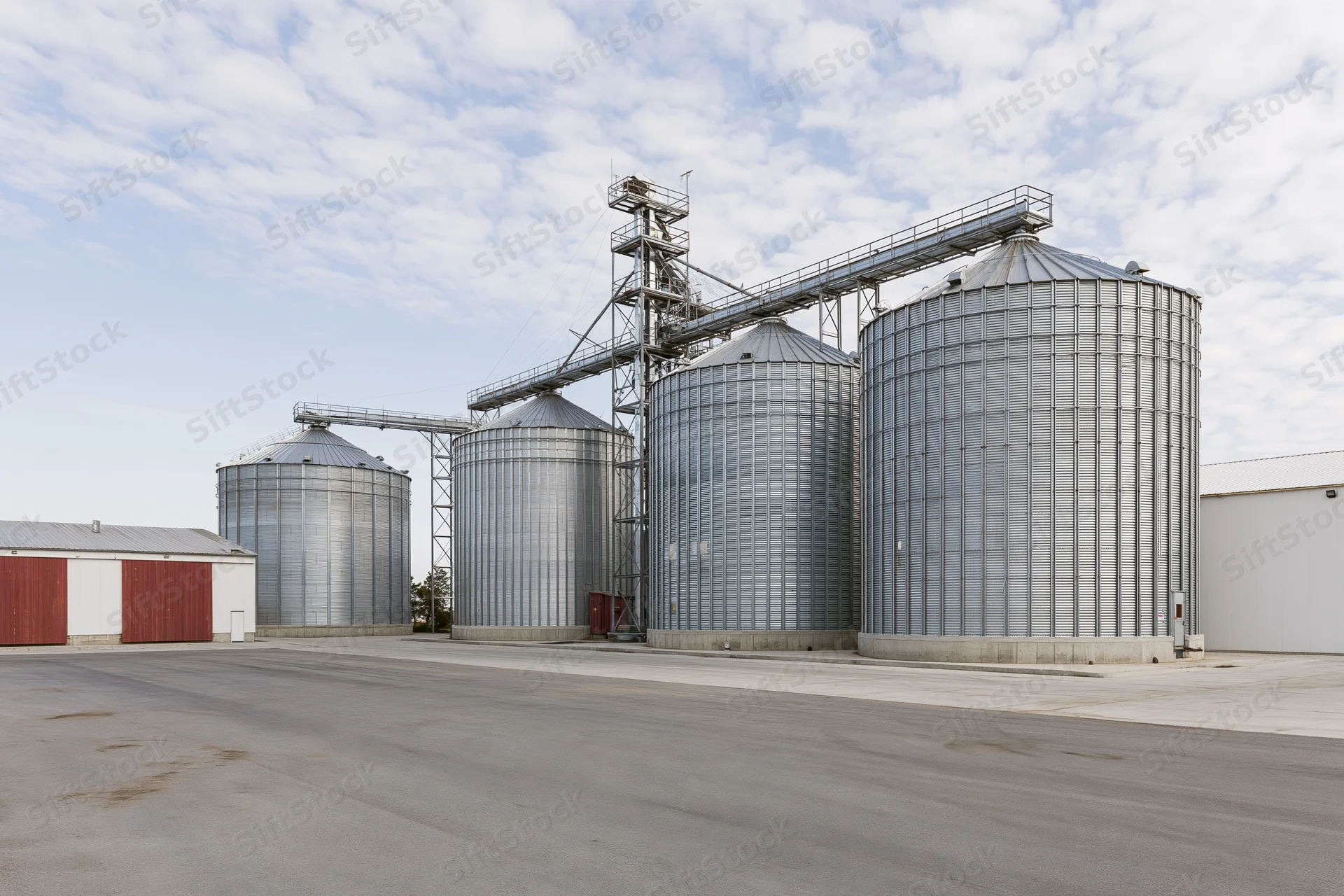 Large grain elevator complex with multiple tall corrugated metal silos under a partly cloudy sky