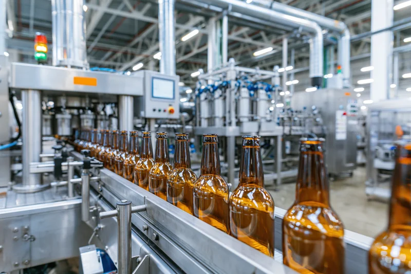 Amber glass beer bottles moving along a conveyor in a large industrial brewery production line