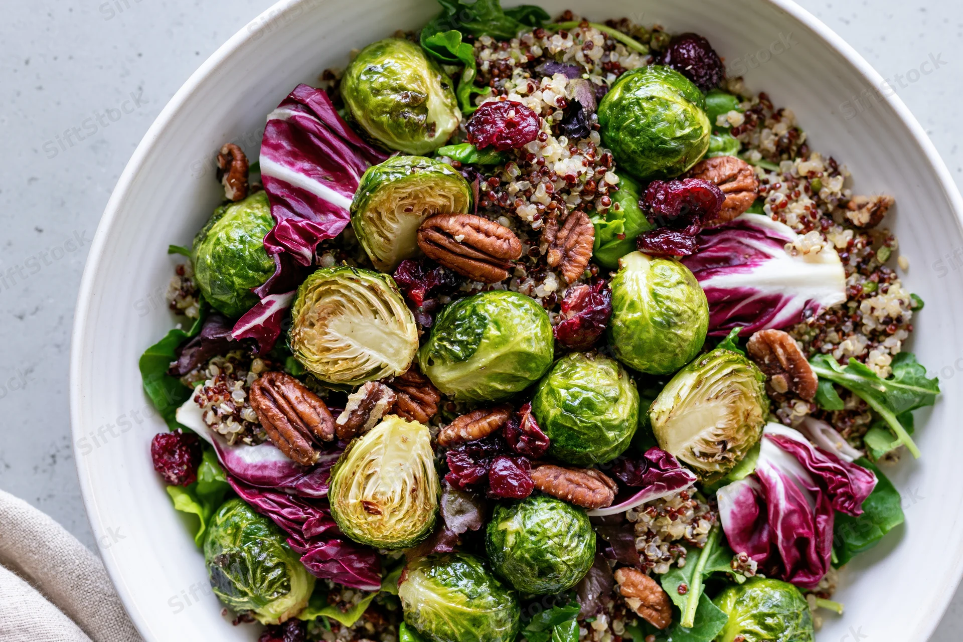 Roasted brussels sprouts salad with quinoa, radicchio, pecans and cranberries in a white ceramic bowl