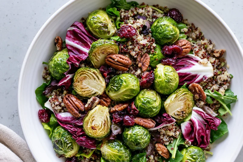 Roasted brussels sprouts salad with quinoa, radicchio, pecans and cranberries in a white ceramic bowl
