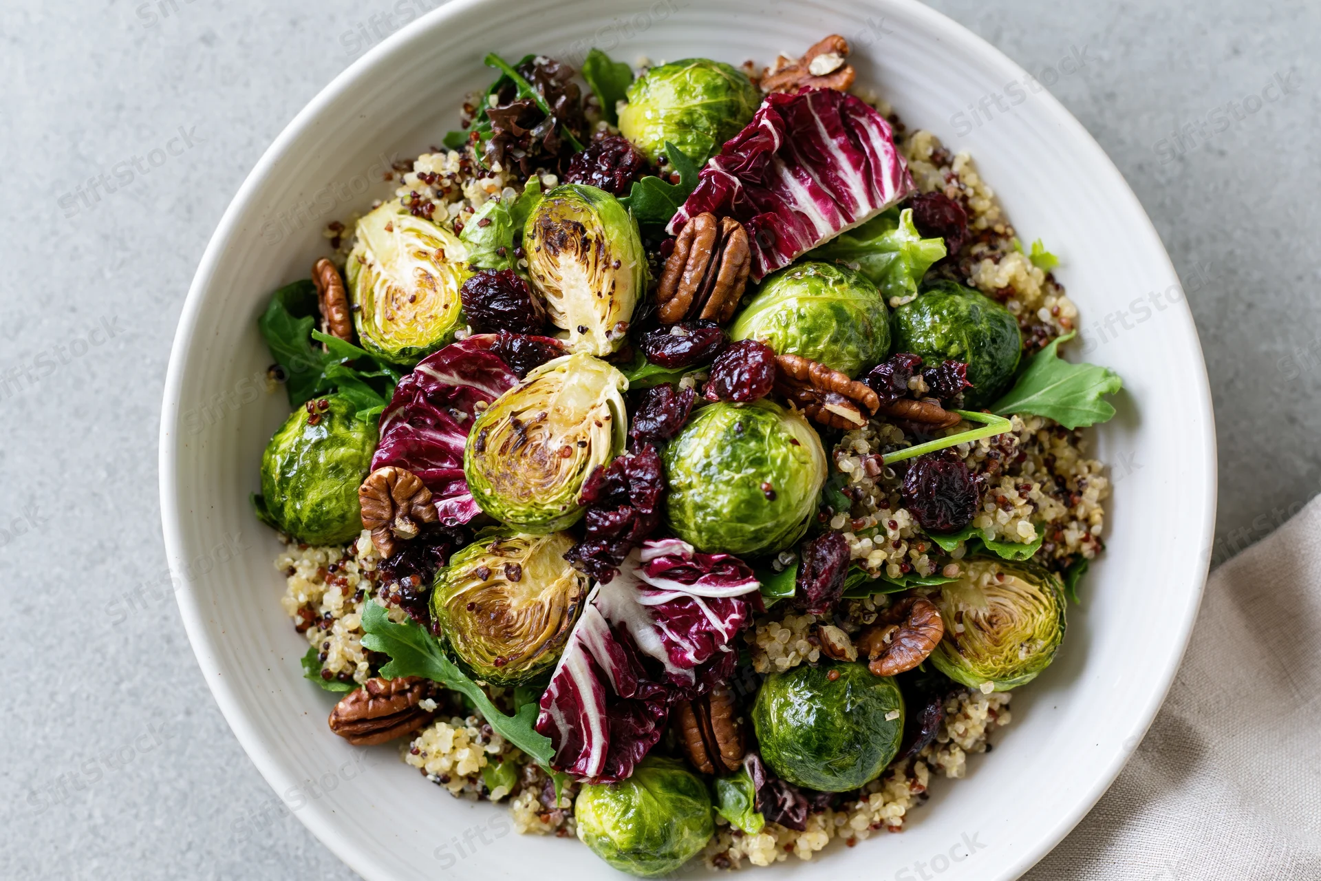 Roasted brussels sprouts salad with quinoa, radicchio, pecans and cranberries in a white ceramic bowl on a gray surface