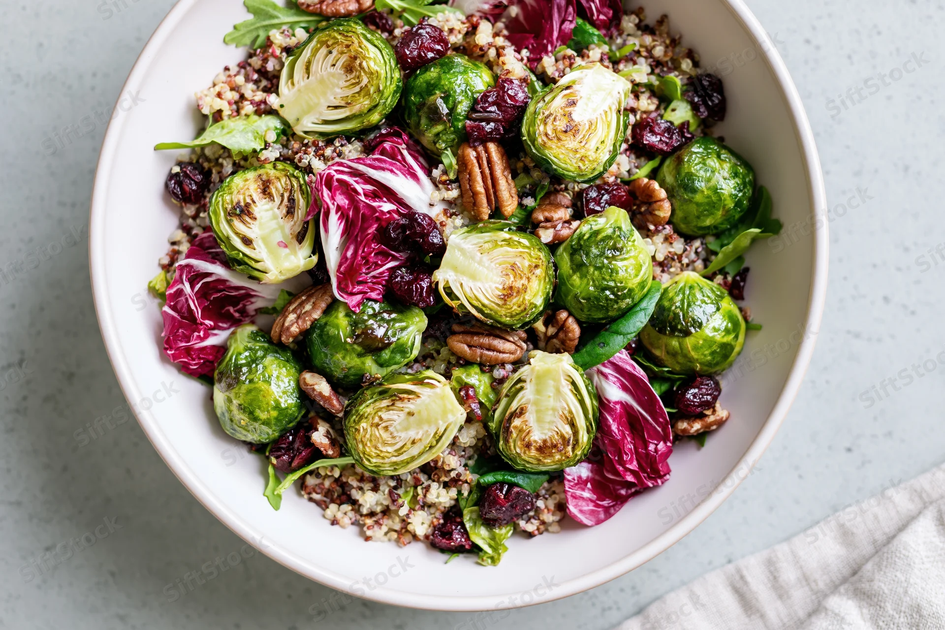 Roasted brussels sprouts salad with quinoa, radicchio, pecans and cranberries in a white ceramic bowl on a gray surface