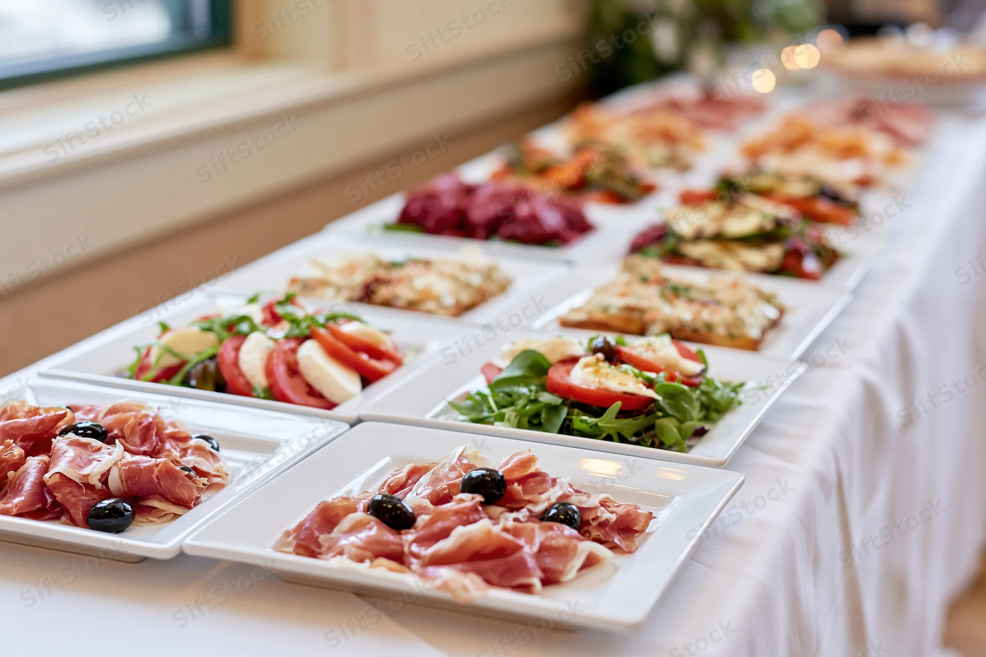 Long banquet table with white linen holding multiple square plates of appetizers arranged in rows