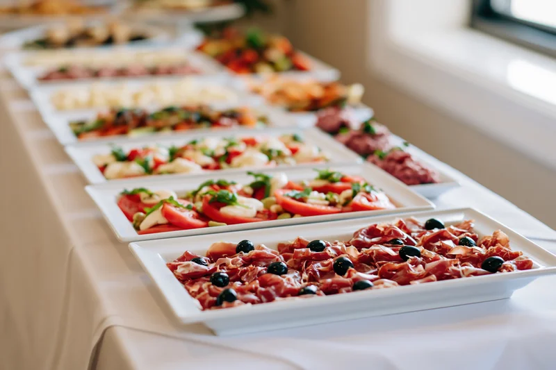 Long banquet table with white linen holding multiple platters of appetizers and salads arranged in rows for a reception event