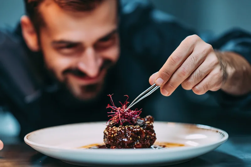 Male chef using tweezers to place garnish on plated dish in restaurant setting