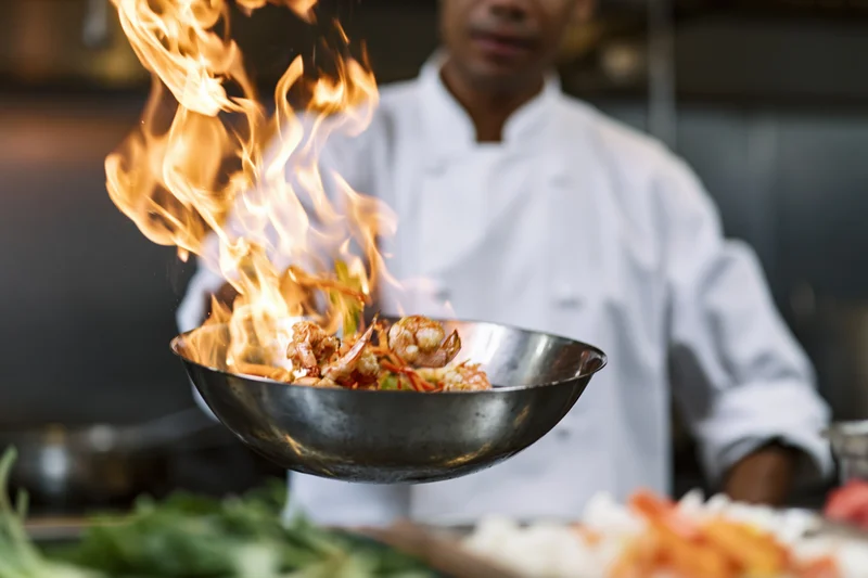Chef flambéing shrimp in a wok in a restaurant kitchen