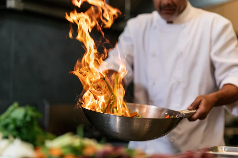 Male chef flambéing shrimp and vegetables in a wok in a restaurant kitchen
