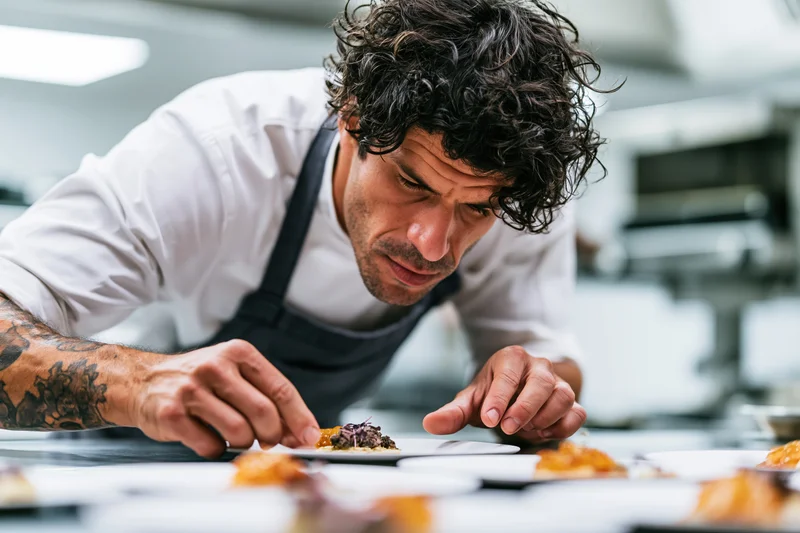 Male chef carefully garnishing a plated dish in a professional kitchen