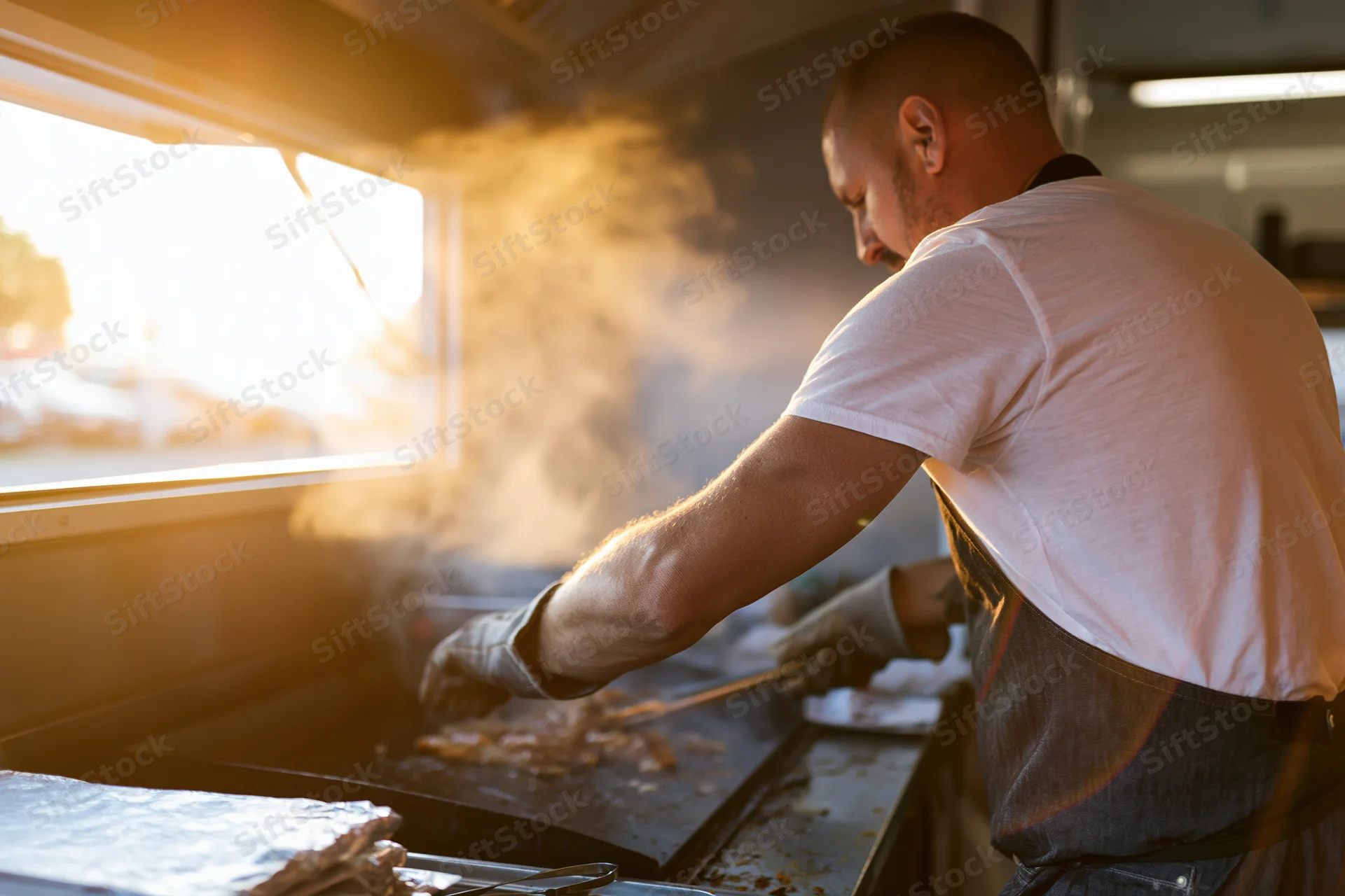 Chef cooking meat on a flat-top griddle inside a food truck kitchen