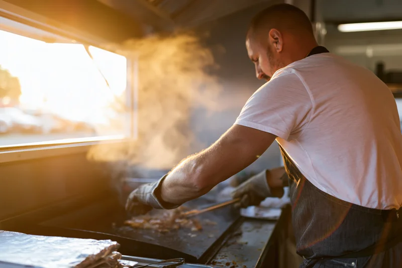 Chef cooking meat on a flat-top griddle inside a food truck kitchen
