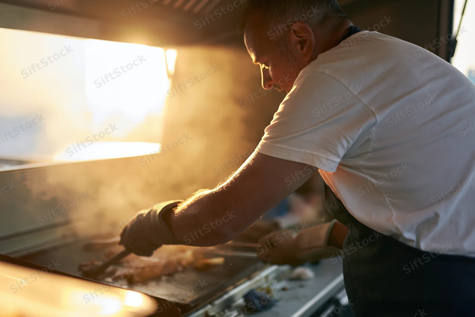 Chef cooking meat on a flat-top griddle in a food truck kitchen