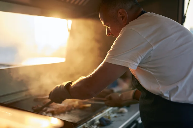 Chef cooking meat on a flat-top griddle in a food truck kitchen