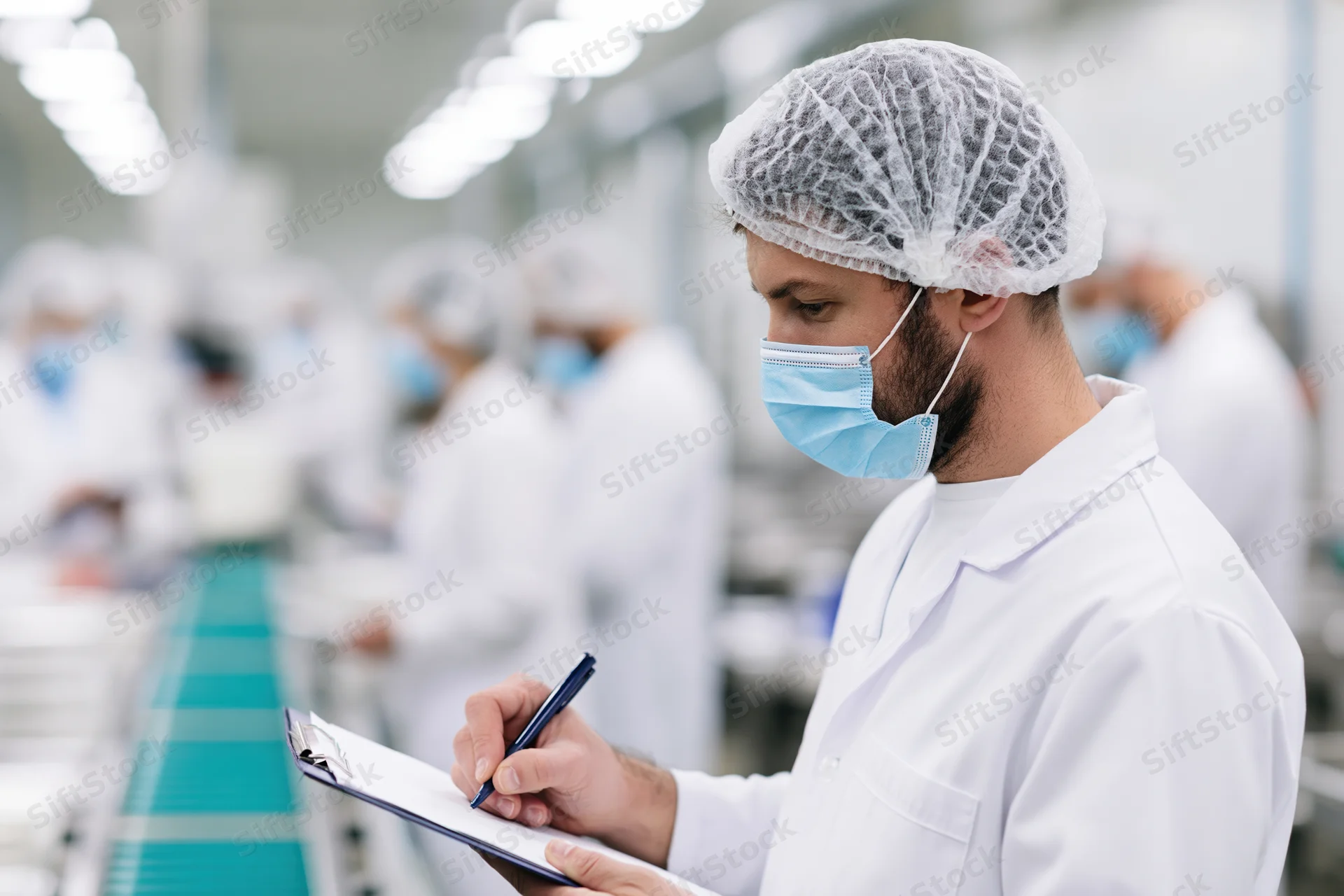 Male quality inspector writing on clipboard in factory cleanroom