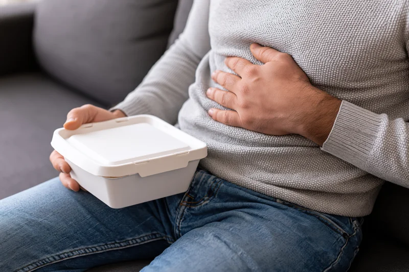 Man holding stomach in discomfort while sitting on couch with takeout container