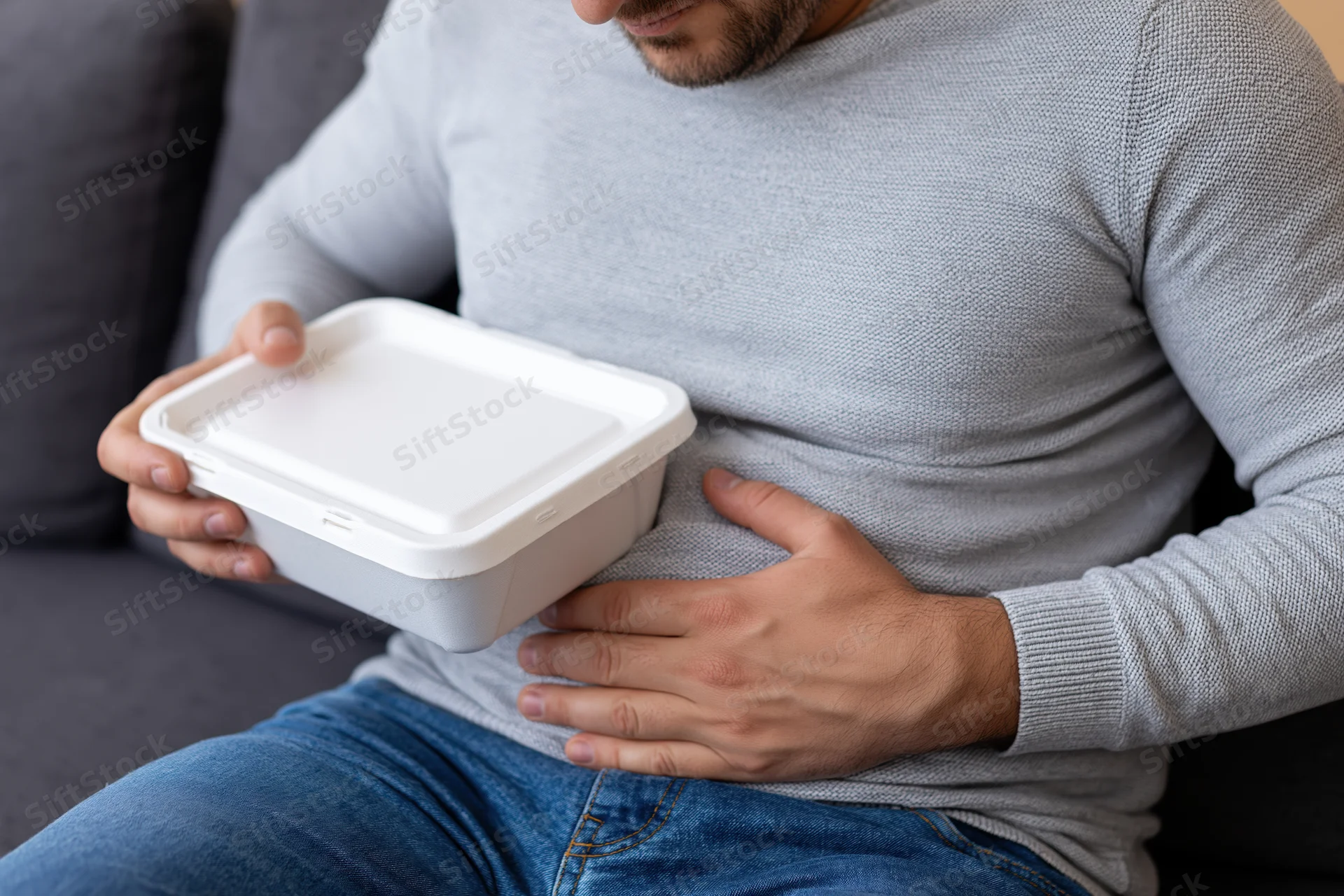 Man holding takeout container and clutching stomach while sitting on couch