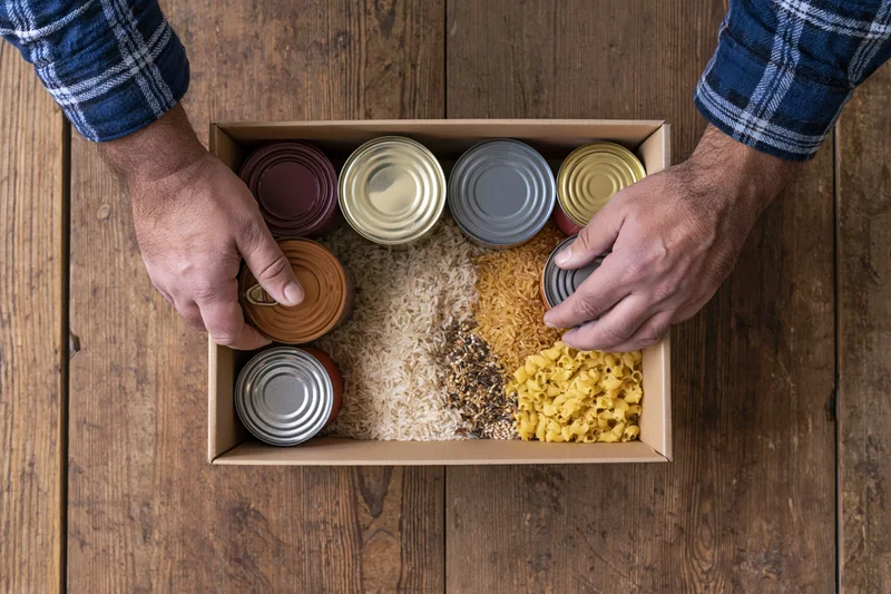 Man arranging canned goods and dry staples in a box on a wooden table