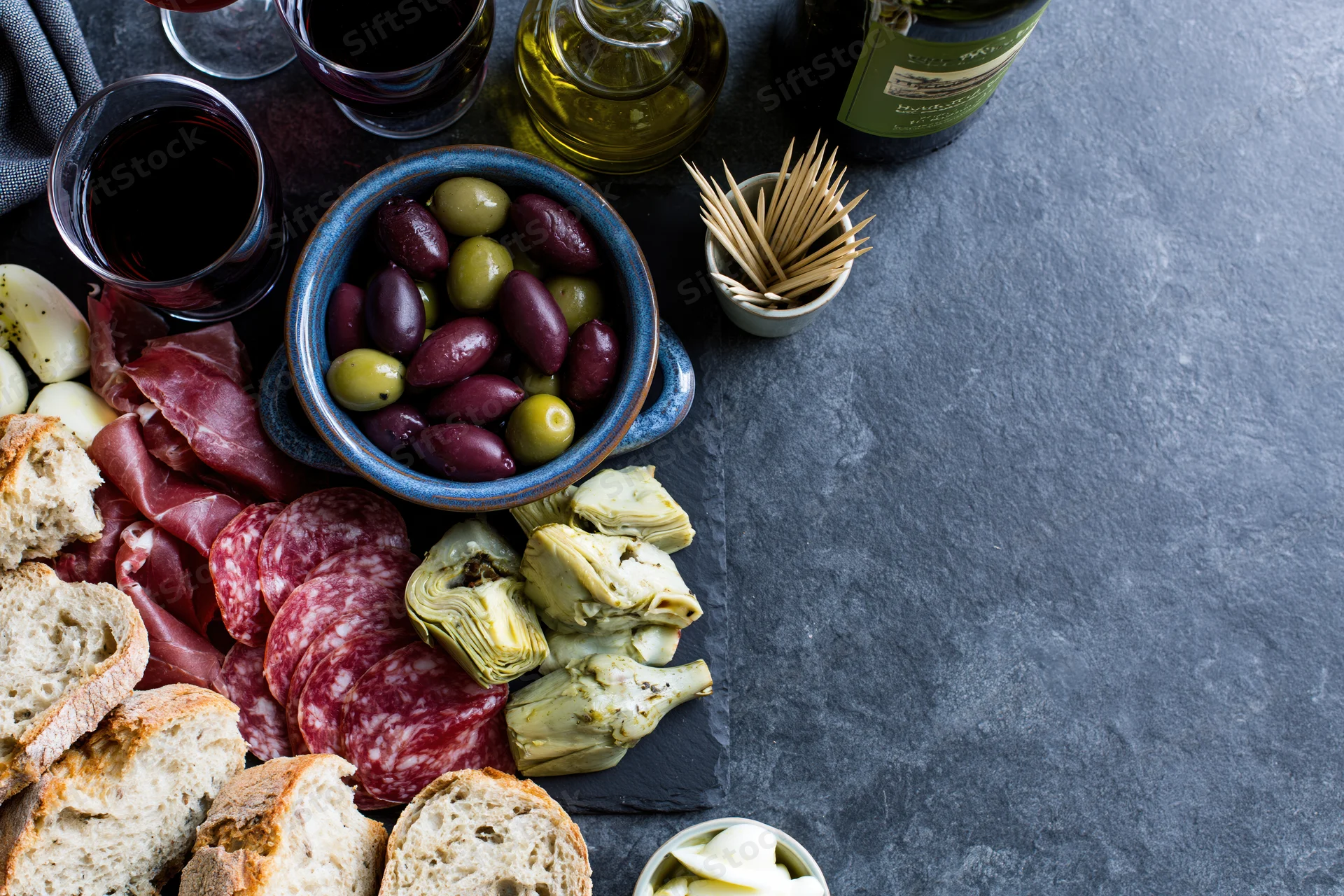 Mediterranean antipasto spread with olives salami artichokes bread and wine on dark slate surface