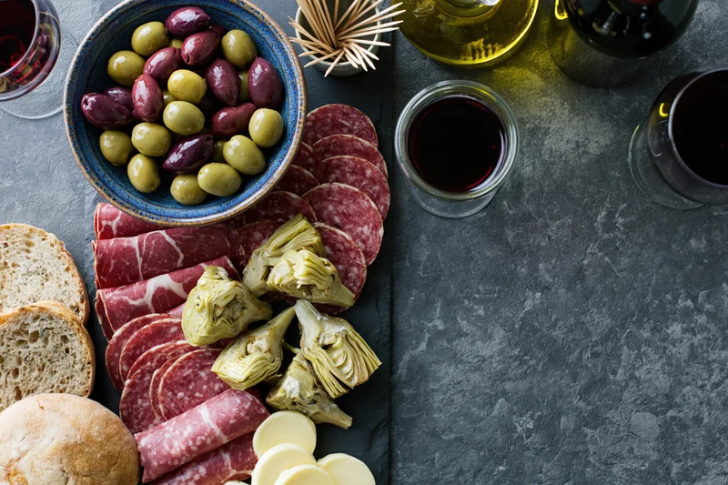 Antipasto spread with salami, olives, artichokes, cheese and bread on a dark slate surface