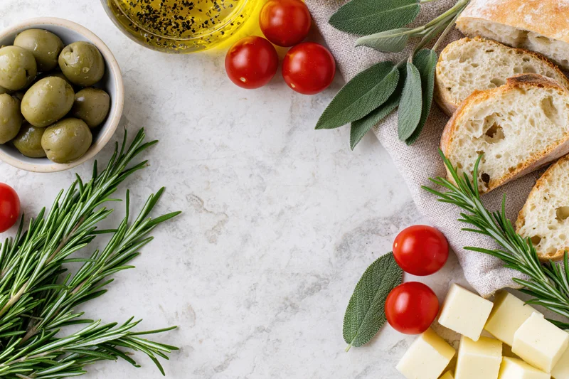Mediterranean food ingredients arranged in a loose border around a white marble surface