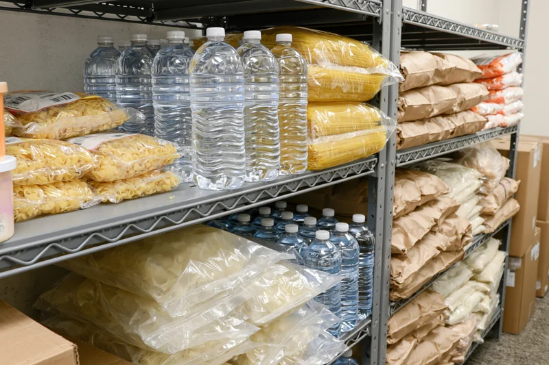 Metal shelving unit stocked with bottled water and dry food supplies in a storage pantry