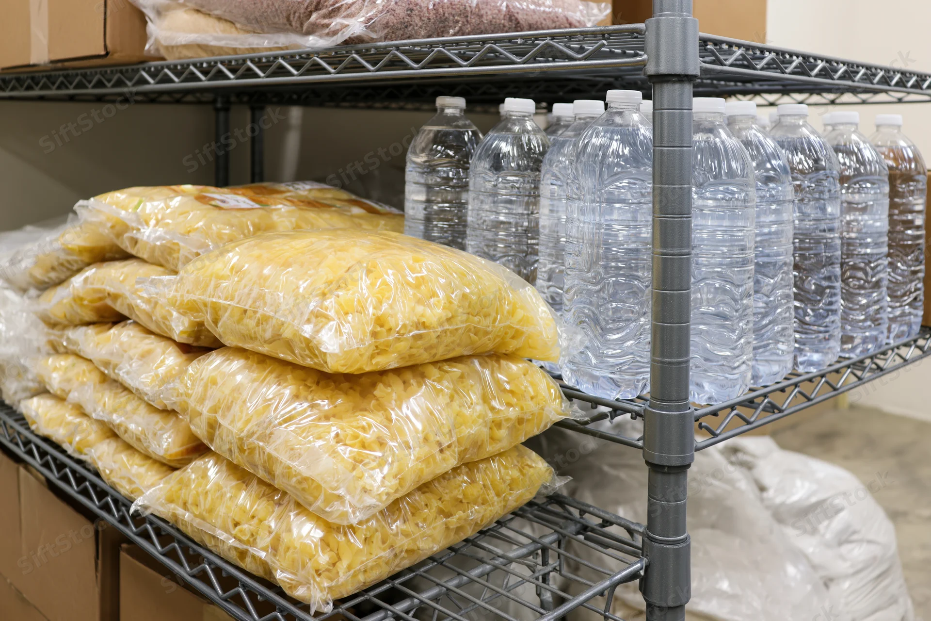 Metal shelving unit holding stacked plastic water bottles and bags of dry pasta in a storage room