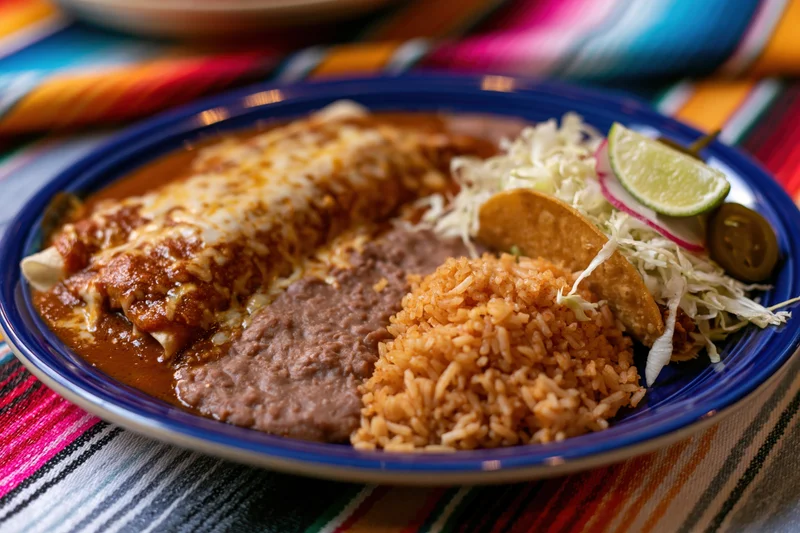 Mexican combination plate with enchilada, rice, beans, and garnishes on a cobalt blue ceramic dish set on a colorful striped textile
