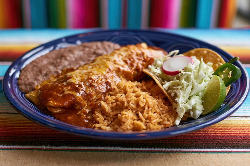 Mexican combination plate with enchilada, rice, beans, and garnishes on a cobalt blue ceramic dish