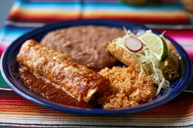 Burrito with rice and beans served on a blue ceramic plate with lime and jalapeno garnish on a striped textile placemat