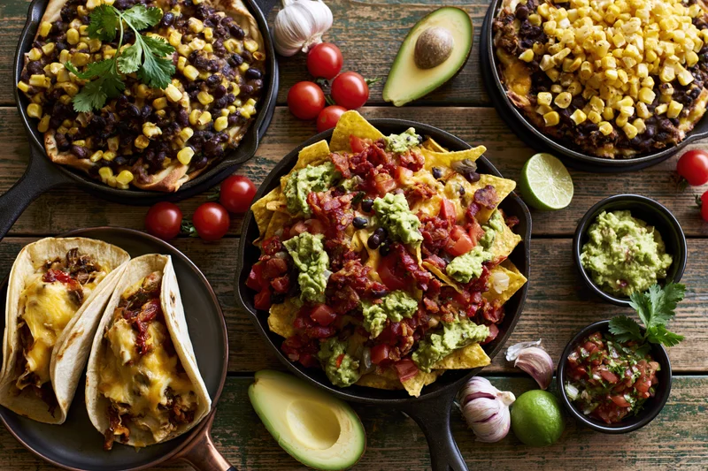 Mexican food spread with nachos, tacos, guacamole and salsa on a wooden table