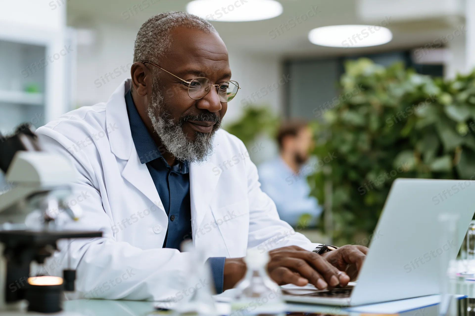 Middle-aged black male scientist in white lab coat typing on laptop in laboratory workspace