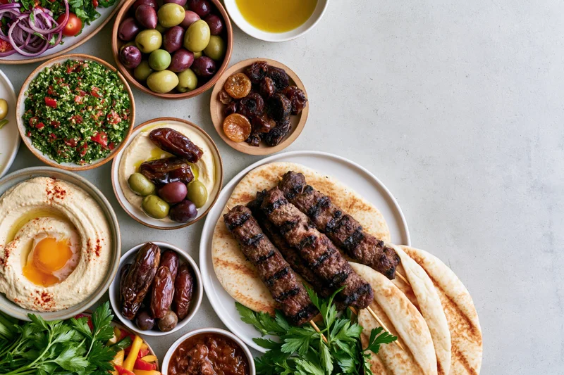 Middle eastern mezze spread with grilled kebabs, hummus, pita, olives and vegetables arranged on a light countertop