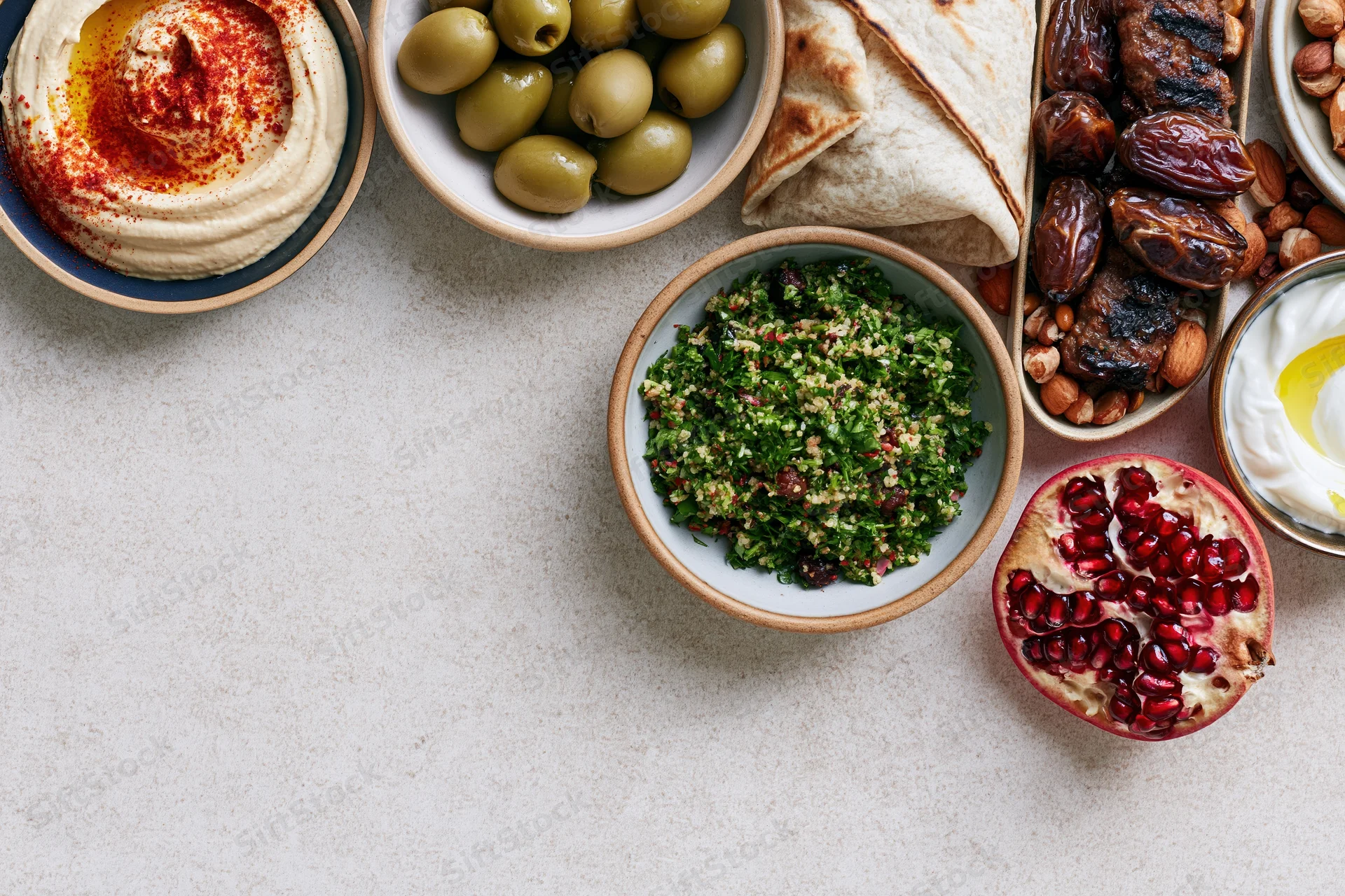Middle eastern mezze spread arranged along the right and top on a light surface with copyspace on the left