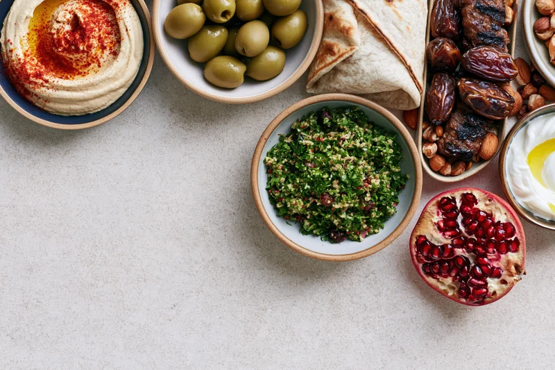 Middle eastern mezze spread arranged along the right and top on a light surface with copyspace on the left
