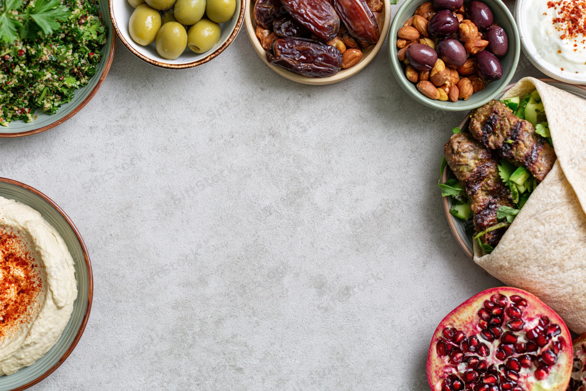 Middle eastern mezze spread arranged along the top and right of a gray table with copyspace in center