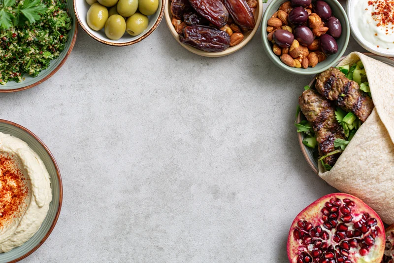Middle eastern mezze spread arranged along the top and right of a gray table with copyspace in center