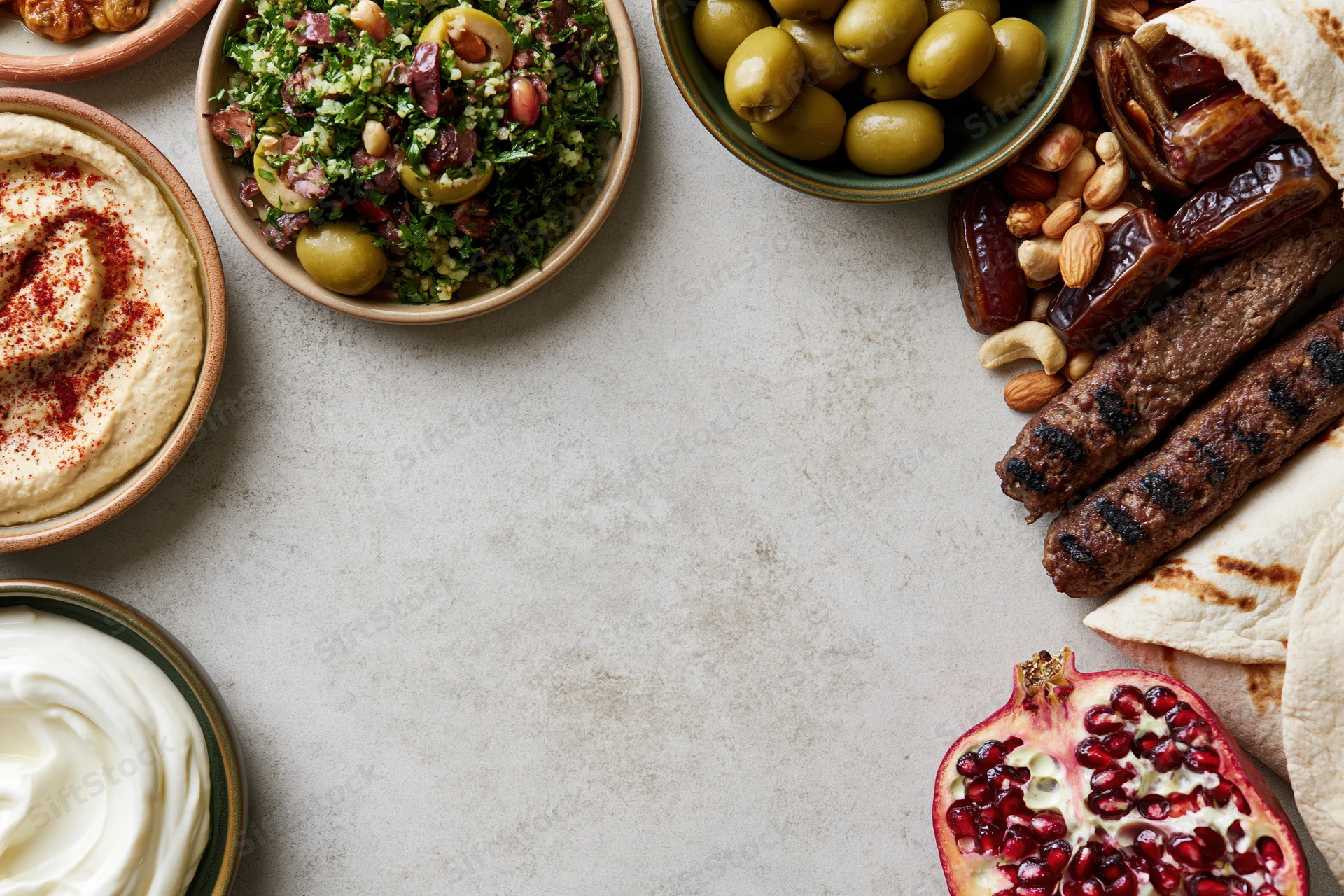 Middle eastern mezze spread arranged along the top and right of a gray stone table with copyspace in center