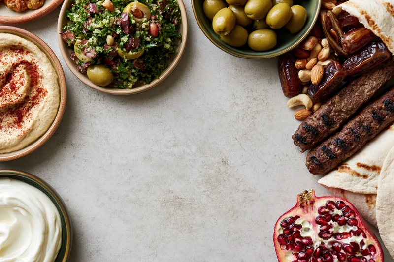 Middle eastern mezze spread arranged along the top and right of a gray stone table with copyspace in center