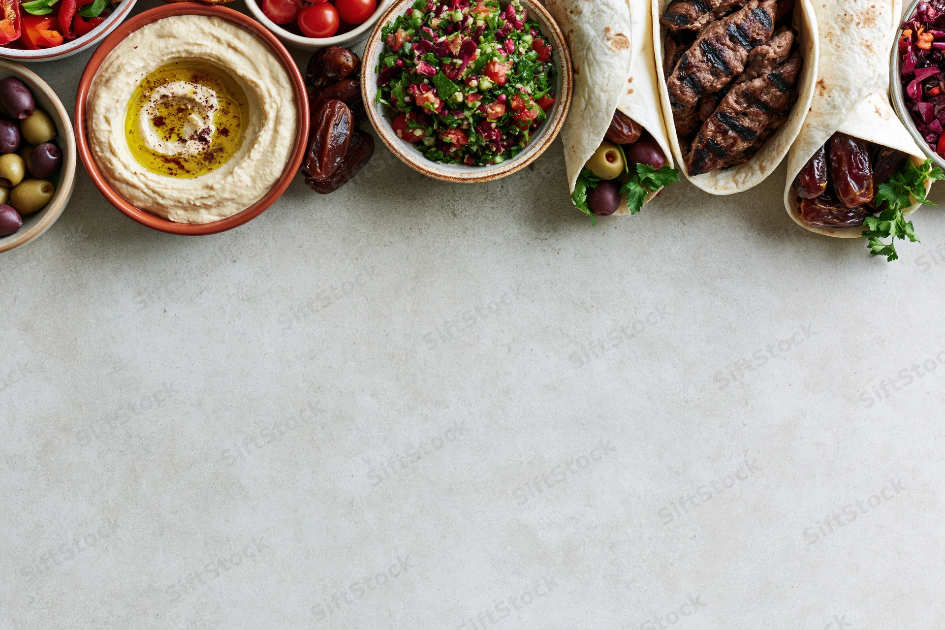 Middle eastern mezze spread arranged along the top edge of a light gray surface with copyspace below