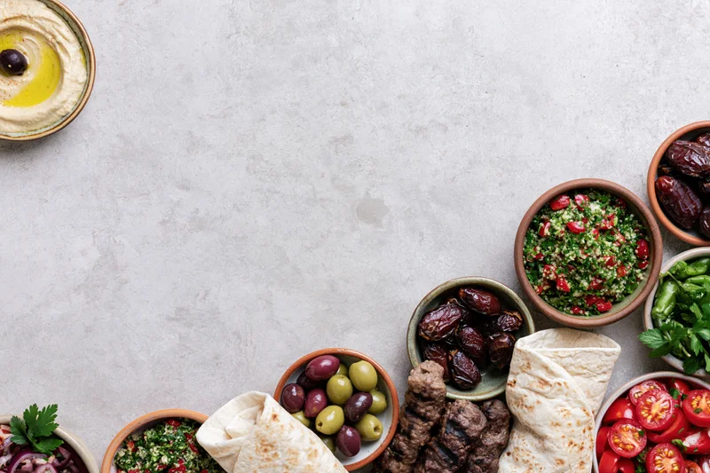 Middle eastern mezze spread arranged along the top edge of a gray stone table with copyspace