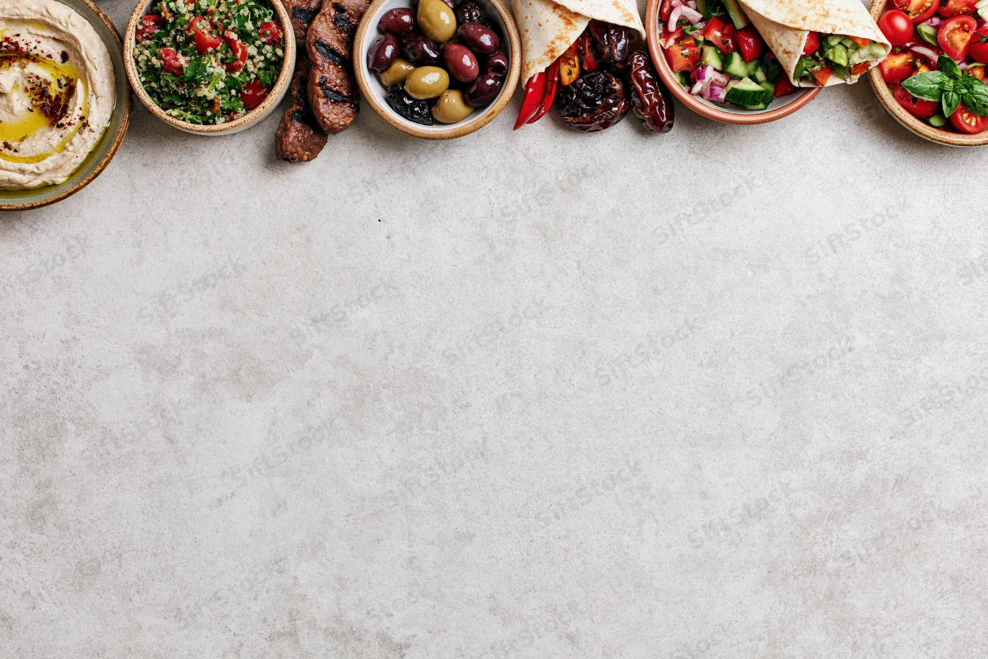 Middle eastern mezze spread arranged along the top edge of a white stone countertop with copyspace below